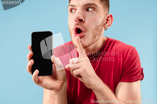 Image of Young handsome man showing smartphone screen isolated on blue background in shock with a surprise face