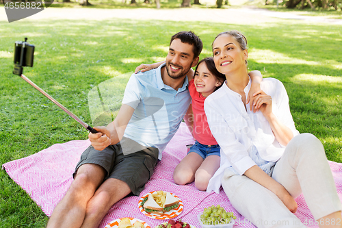 Image of family having picnic and taking selfie at park