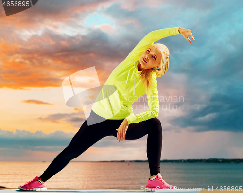 Image of woman stretching on exercise mat at seaside