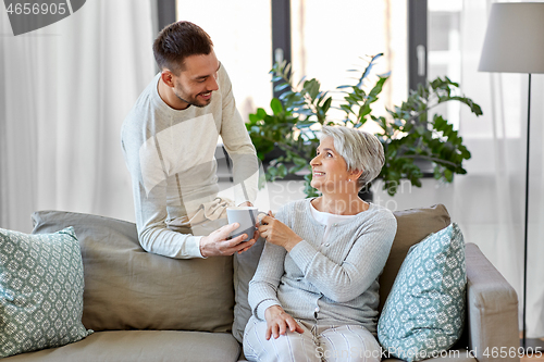 Image of adult son bringing coffee to senior mother at home