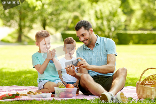 Image of family with smartphone having picnic at park
