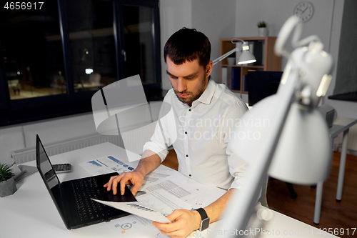 Image of businessman with papers and laptop at night office