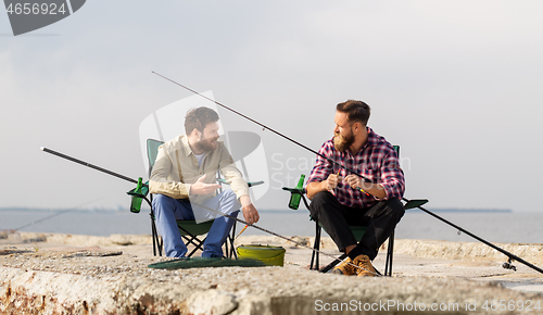 Image of friends adjusting fishing rods with bait on pier