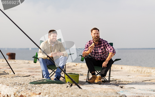 Image of happy friends fishing and eating sandwiches