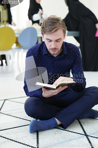 Image of young muslim man reading Quran at home