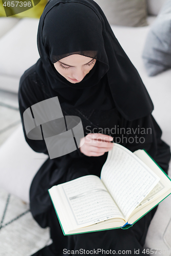 Image of young muslim woman reading Quran at home