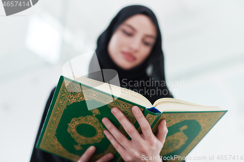 Image of young muslim woman reading Quran at home