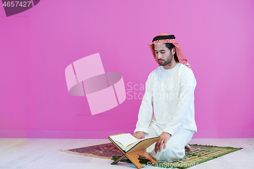 Image of young arabian muslim man reading Quran at home