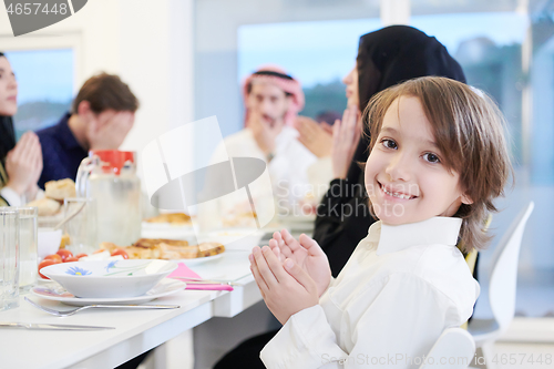 Image of little muslim boy praying with family before iftar dinner