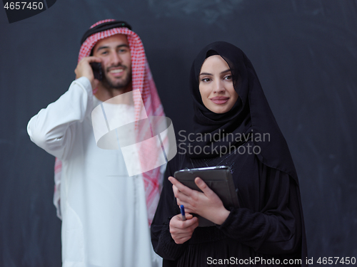 Image of muslim couple using modern technology in front of black chalkboa