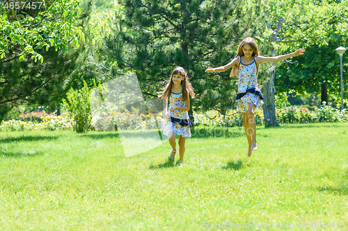 Image of Two girls have fun running on the green lawn in the park