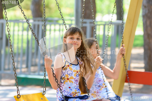 Image of Two girls swing on a swing in a city park