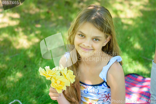 Image of A tousled girl sits in a clearing and holds a bouquet of yellow roses