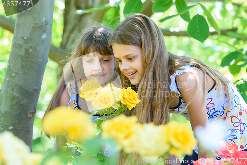 Image of Two girls enjoy the beauty of yellow roses in the garden