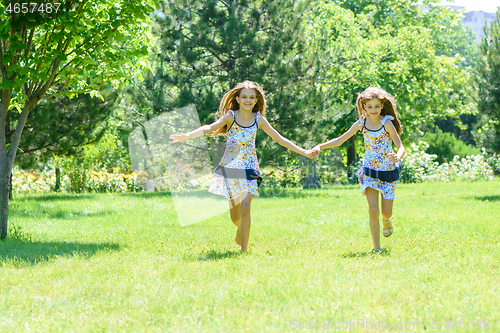Image of Two girls holding hands run on a green lawn in a park