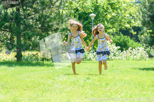 Image of Two little sister run on a green lawn in a park