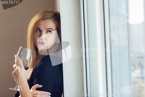 Image of portrait of a girl looking sadly out the window with wine in her hands