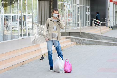 Image of a man in a medical mask stands on the street shopping and talks on his mobile phone