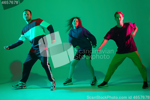 Image of Stylish men and woman dancing hip-hop in bright clothes on gradient background at dance hall in neon light