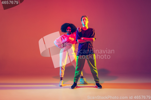 Image of Stylish man and woman dancing hip-hop in bright clothes on gradient background at dance hall in neon light