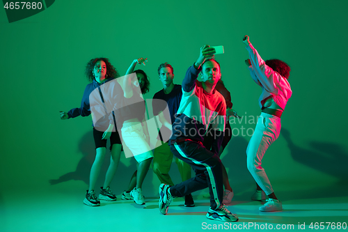 Image of Stylish men and woman dancing hip-hop in bright clothes on gradient background at dance hall in neon light