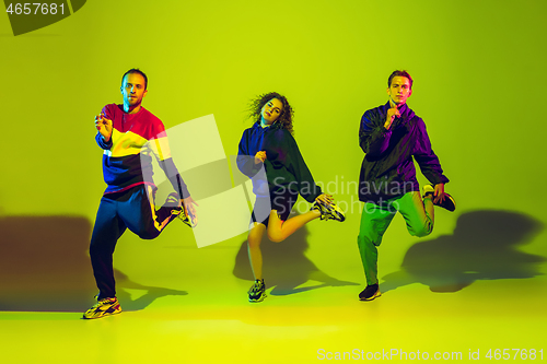 Image of Stylish men and woman dancing hip-hop in bright clothes on gradient background at dance hall in neon light