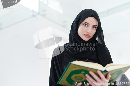 Image of young muslim woman reading Quran at home