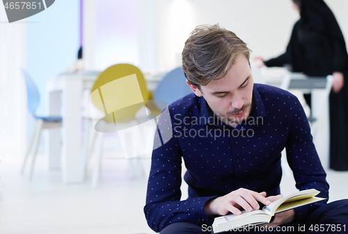 Image of young muslim man reading Quran at home