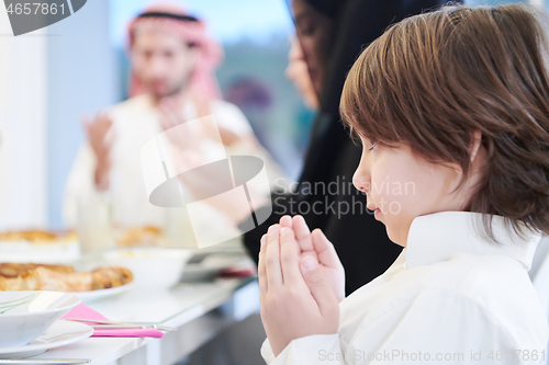 Image of little muslim boy praying with family before iftar dinner