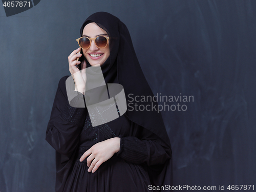 Image of young muslim woman wearing sunglasses using smartphone