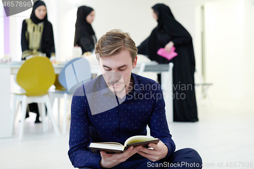 Image of young muslim man reading Quran at home