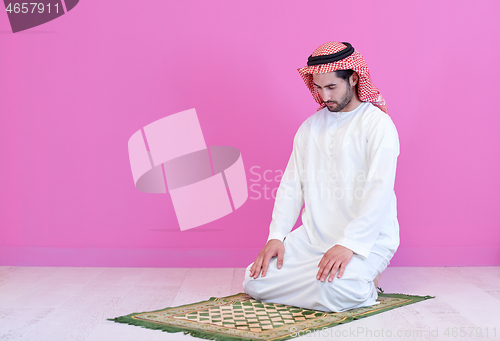 Image of young arabian muslim man praying on the floor at home