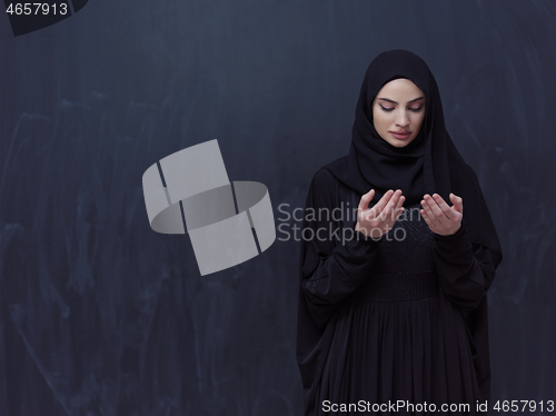 Image of muslim woman making traditional prayer to God in front of black 