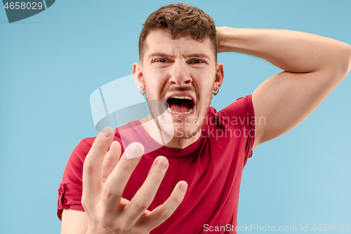 Image of The young emotional angry man screaming on blue studio background