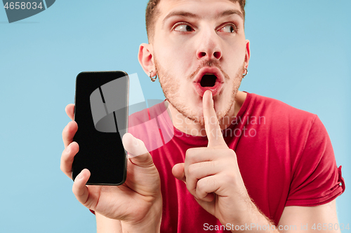 Image of Young handsome man showing smartphone screen isolated on blue background in shock with a surprise face