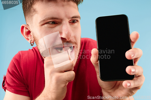 Image of Young handsome man showing smartphone screen isolated on blue background in shock with a surprise face