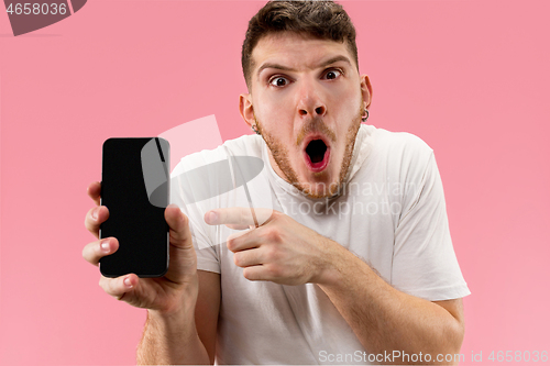 Image of Young handsome man showing smartphone screen isolated on pink background in shock with a surprise face