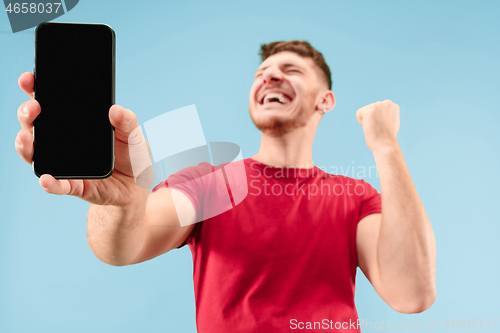 Image of Young handsome man showing smartphone screen isolated on blue background in shock with a surprise face