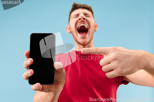 Image of Young handsome man showing smartphone screen isolated on blue background in shock with a surprise face