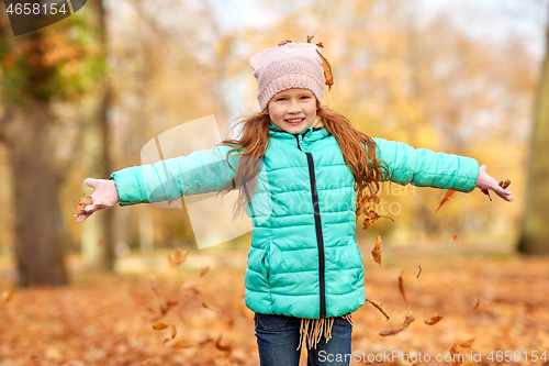 Image of happy girl playing with leaves at autumn park