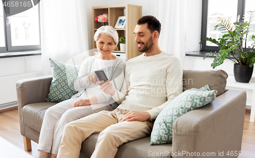 Image of old mother and adult son with smartphone at home