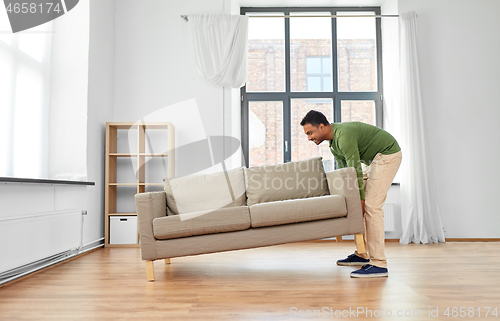 Image of happy indian man moving sofa at home