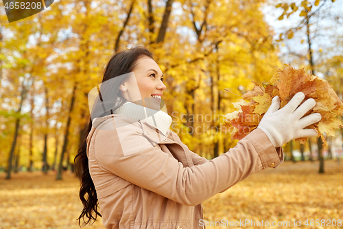 Image of happy woman having fun with leaves in autumn park