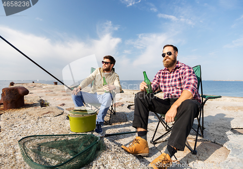 Image of male friends fishing and drinking beer on sea pier