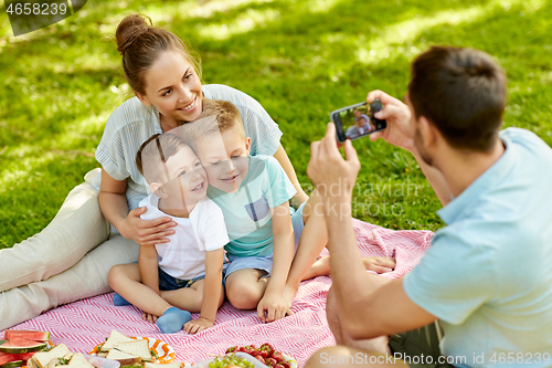 Image of father taking picture of family on picnic at park