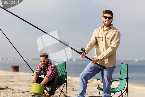 Image of male friends with fishing rods on sea pier