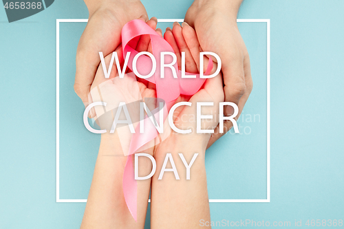 Image of the text world cancer day and a pink ribbon on a table background