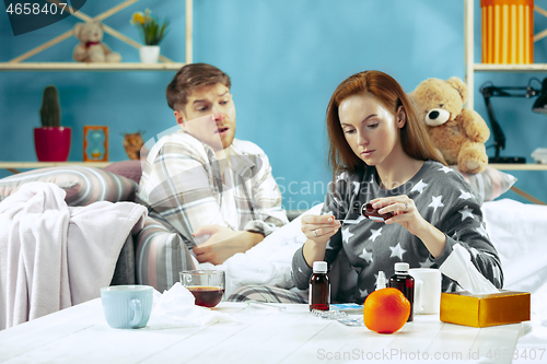 Image of Sick man with fever lying in bed having temperature girl take care for him