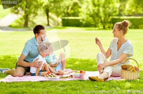 Image of mother taking picture of family on picnic at park