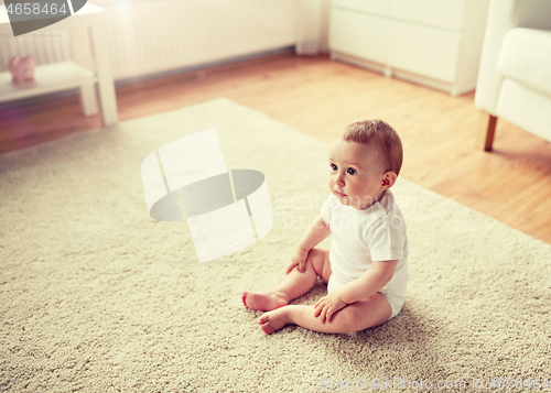 Image of happy baby boy or girl sitting on floor at home